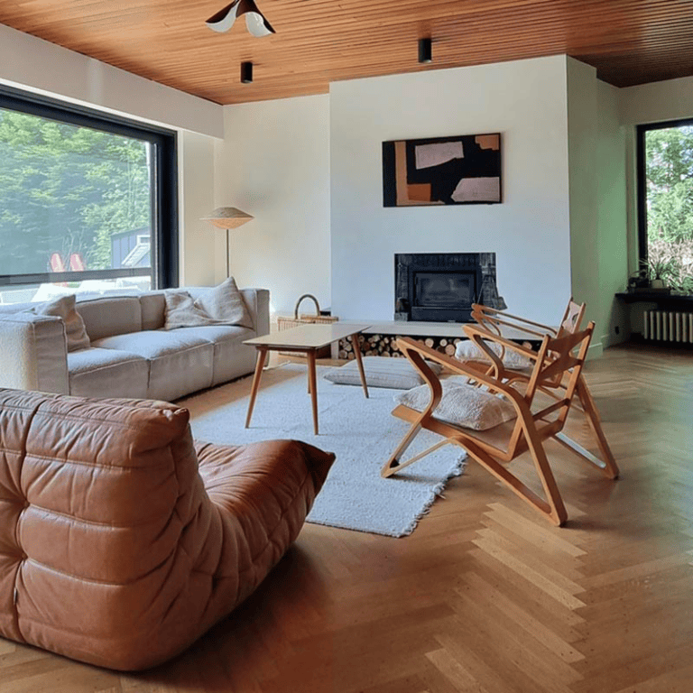 Un salon chaleureux, avec des assises confortables au milieu de la pièce éclairée par deux grandes baies vitrées.